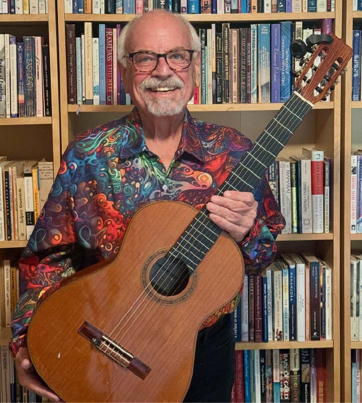Ron Franklin holding a classical guitar in front of a wall of books.